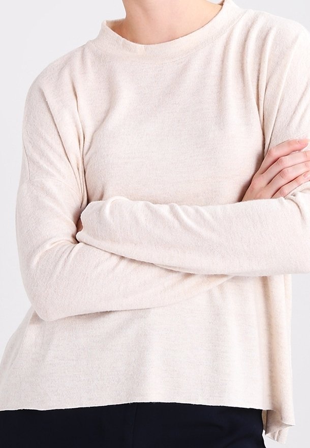 Ljust beige långärmad tröja med hög krage, avslappnad passform och mjuk textur; har sänkta axlar och slitsar på sidorna vid fållen.