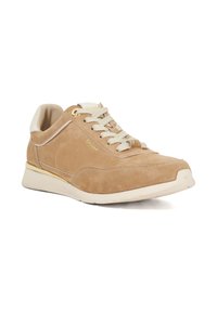 Beige suede sneaker with a smooth toe cap, padded collar, and beige laces. Features a gold accent and a cushioned white sole.