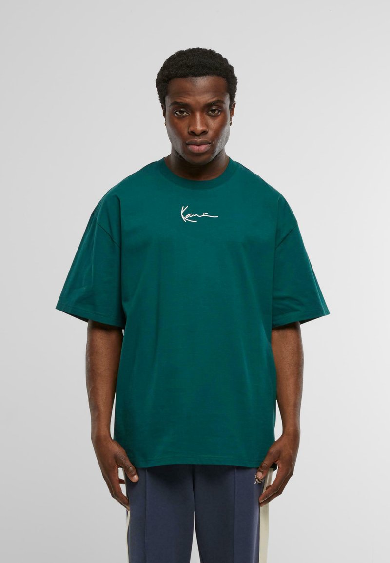 Tricou din bumbac teal, cu mâneci scurte, guler rotund și un logo alb brodat pe piept. Design simplu și croială lejeră.