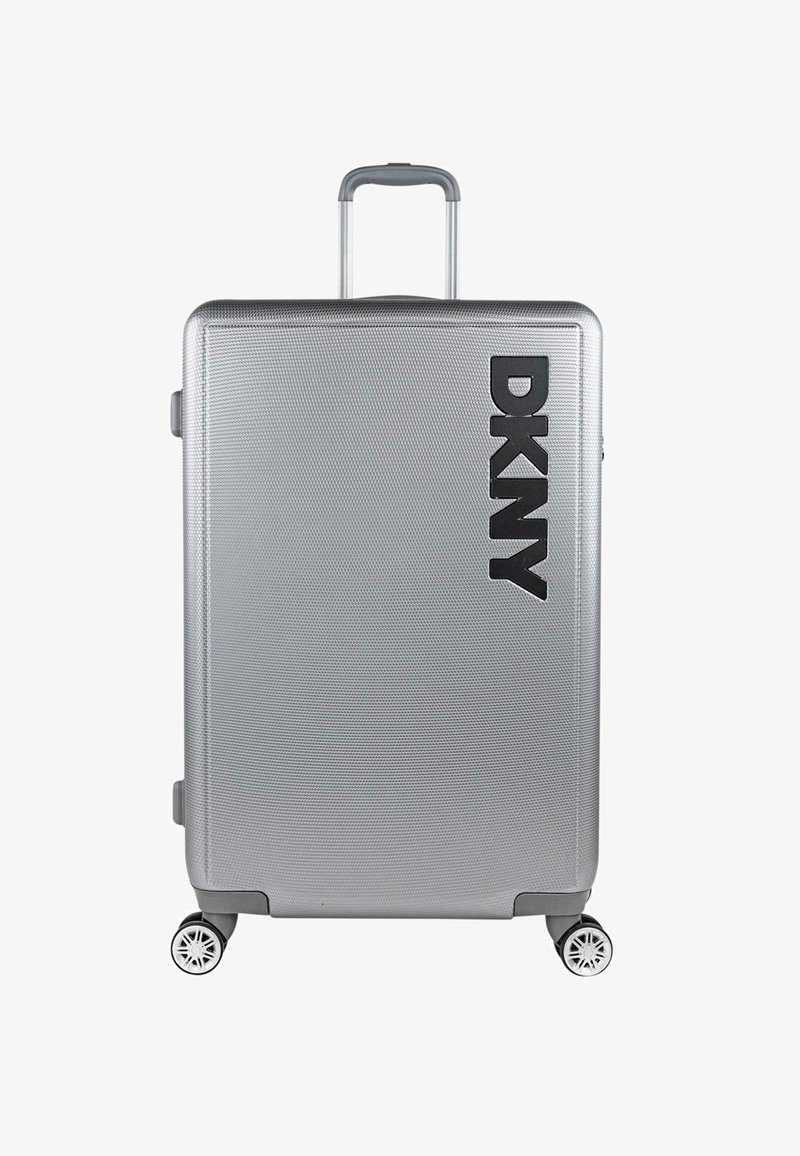 Maleta rígida plateada con superficie texturizada, que presenta un prominente logo negro de DKNY, un asa retráctil y cuatro ruedas multidireccionales.