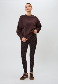 Dunkelbrauner übergroßer Sweatshirt, schwarze Leggings mit Leopardenmuster und braune Sneakers mit rosa Akzenten. Weicher Stoff und taillierte Passform.