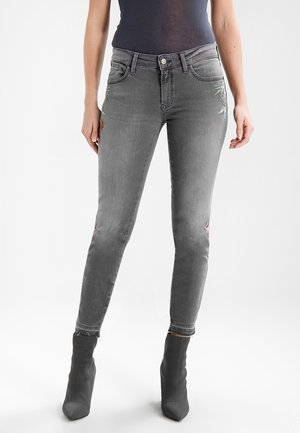 Jeans de mezclilla gris de corte slim, con bordados florales en los muslos y detalles desgastados cerca do do do do do do. Combinados con botas de tobillo grises.