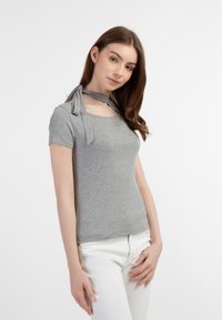 Lys grå ribbede t-shirt med korte ærmer, der har et choker-lignende halsbånd og en tætsiddende pasform. Sammen med hvide bukser.