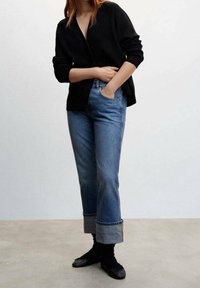 Černý kardigan s výstřihem do V, doplněný o světle modré riflové džíny se sklopeným lemem. Černé ponožky a ploché boty dotvářejí celý outfit.