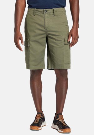Cargo-Shorts aus olivgrünem Baumwollmaterial mit Seitentaschen, einem normalen Bund und geradem Schnitt, kombiniert mit schwarz-braunen Sneakern.