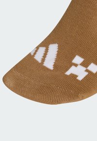 Brązowa skarpeta z teksturowanym wzorem, z białym logo nadrukowanym w okolicy palców. Zaokrąglony czubek i gładkie wykończenie.