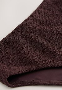 Gros plan d'un tissu brun foncé texturé avec un motif tricoté ondulé en relief et une doublure lisse visible au bord.