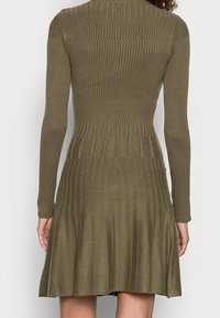Abito in maglia di un verde oliva con maniche lunghe, texture a coste e gonna a ruota. Presenta dettagli a coste orizzontali e verticali.