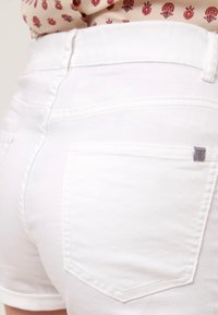 Valkoiset farkkushortsit takataskuilla, joissa on pieni harmaa logo-tägi oikeassa taskussa. Silkkinen pinta ja istuva malli.