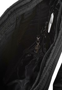 Interior de una bolsa de tote de tela negra con una textura suave, que cuenta con un lazo para llavero y una etiqueta blanca en un bolsillo lateral.