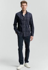 Marineblaue Karobluse zum Knöpfen, lange Ärmel, lockere Passform, kombiniert mit dunkler Hose und weißen Turnschuhen, mit Brusttasche und dezenter Textur.