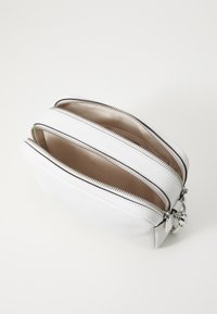 Vit läderväska med tre dragkedjefack, strukturerad yta, silverfärgad detalj och en slät beige inredning. Kompakt design.