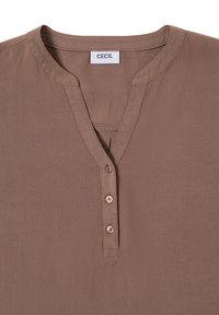 Hnědá blůza s výstřihem do V, obsahující knoflíkovou lištu se třemi knoflíky. Látka je hladká a štítek říká "CECIL."