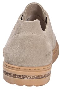 Chaussure en daim beige avec un dos arrondi et un design découpé. Dispose d'une semelle en caoutchouc beige avec un accent texturé près de la base.