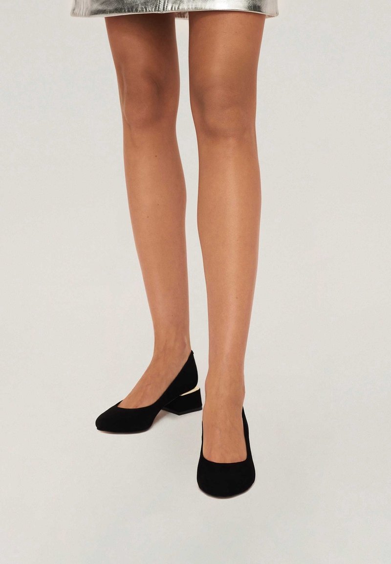 Chaussures à talons carrés en daim noir avec un design à bout pointu, comprenant un petit accent doré à l'arrière. Texture lisse, silhouette élégante.