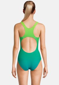 Groene en blauwe gestreepte bikini met een racerback ontwerp en grote uitsparing op de rug. Het materiaal lijkt glad en rekbaar.