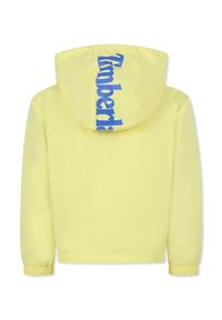 Giacca leggera gialla con un logo blu sul cappuccio. Ha una texture liscia, polsini elastici e un cappuccio regolabile con cordino.