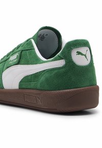 Vihreät mokkanahkakengät, joissa on valkoiset nahka-accentit, pehmustettu kaulus, ruskea kumipohja ja Puma-logo kantapäällä ja sivussa. Klassinen matalamallinen muotoilu.