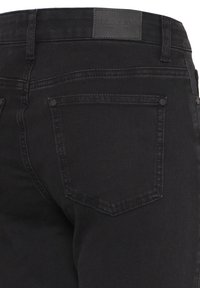 Zwarte spijkerbroek met achterzak en riemlussen, voorzien van een gestikte leren merkembleem op de tailleband.