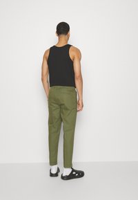 Débardeur noir, pantalon vert olive avec revers roulés, chaussettes blanches et chaussures noires. Texture lisse, coupe ajustée. Vue de dos de la tenue.