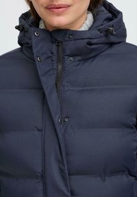 Navy blue puffer jacket with a hood, featuring a front zipper, snaps, and quilted sections. Soft texture with a matte finish.