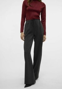 Pantalons large gris foncé avec une taille à cordon de serrage. Associés à un haut bordeaux à manches longues texturé présentant des motifs verticaux.