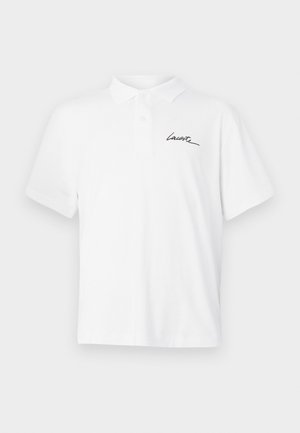 Hvit polo skjorte laget av bomull, med spiss krage, tre knapper i midten og svart kursiv logo på venstre bryst.