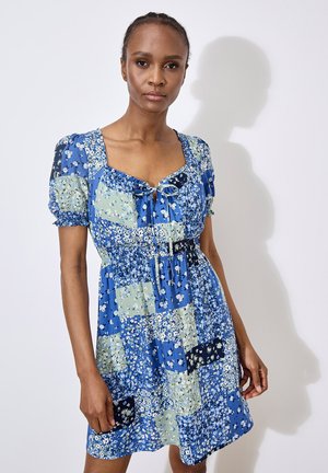 Blaues Blumen-Patchwork-Kleid mit kurzärmeligen Puffärmeln, quadratischer Ausschnitt, taillierter Taille und Bindeband-Detail an der Vorderseite, gefertigt aus leichtem Stoff.