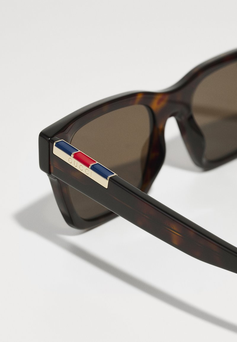  Schildpad-design zonnebril met bruine lenzen. De zijden zijn voorzien van gouden hardware met blauwe en rode accenten. Vierkante monturen zorgen voor een gedurfde uitstraling.