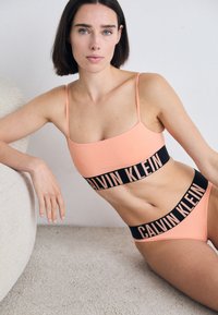 Perzik kleur bralette en bikini set met zwarte "CALVIN KLEIN" branding. Gladde textuur, minimalistisch ontwerp en dunne verstelbare bandjes.