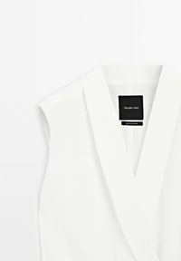 Vit ärmlös topp med V-ringning, tillverkad av mjukt tyg, har ett inre foder och en etikett som visar "Massimo Dutti."