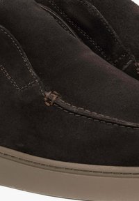 Czarne zamszowe buty wsuwane z okrągłym noskiem, kontrastowymi szwami i gumową podeszwą. Posiadają dekoracyjny detal w postaci przeszyć.