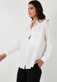 White long-sleeve button-up shirt with chest pockets, made of lightweight fabric. Features a classic collar and a relaxed fit.