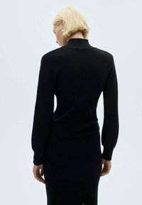 Maglione nero a maglia con maniche lunghe e colletto alto, caratterizzato da una texture a coste e un design aderente. Nessun abbellimento visibile.