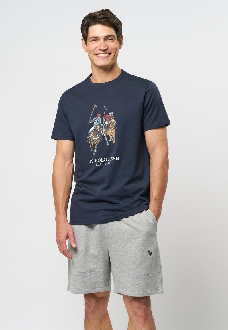 Jūrų jėgos T-marškiniai su polokrančio grafika daugiaspalviu dizainu ir užrašu "U.S. POLO ASSN. Nuo 1890 metų." Su pilkais šortais, faktūruota medžiaga.