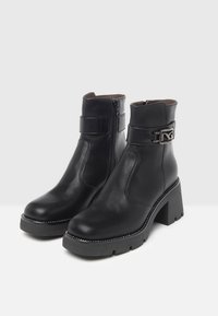 Black leather ankle boots with a chunky heel, side zipper, metal buckle accent, and contrasting white stitching along the sole.
