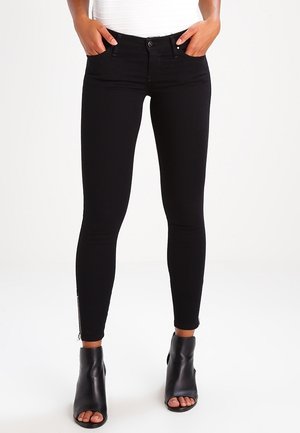 Los pantalones vaqueros negros ajustados cuentan con un diseño ceñido, bolsillos delanteros y un detalle de cremallera en el tobillo. Están hechos de un material de mezclilla elástico.
