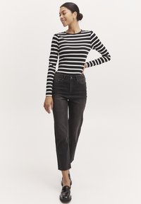 Schwarz-weißer gestreifter Langarmoberteil kombiniert mit dunklen hoch taillierten Jeans. Die Jeans haben einen rohen Saum und das Outfit wird mit schwarzen Loafers vervollständigt.