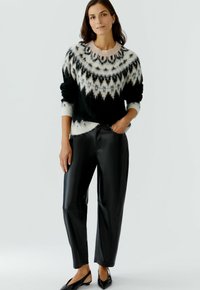 Pull en maille à motifs noir et blanc avec un col rond, associé à un pantalon en simili cuir noir brillant et des chaussures plates noires.