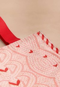 Czerwono-różowa torba na ramię z teksturowanym materiałem w serca, z płaskim, wstążkowatym uchwytem i przeszytymi detalami wzdłuż krawędzi.