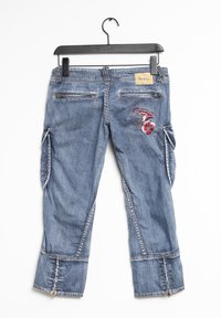 Pantalones cargo de mezclilla azul con diseño floral bordado, múltiples bolsillos y cremalleras en el dobladillo. Cuelga de una percha de plástico negra.