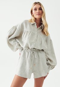 Světle šedá lněná košile s plisé detaily, knoflíky a šortky s elastickým pasem. Měkká textura, uvolněný střih a akcenty se stahovací šňůrkou.
