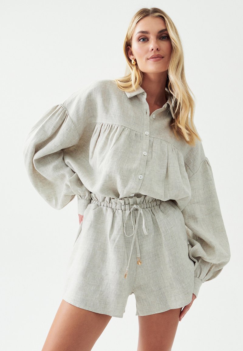 Lichtgrijze linnen shirt met geplooide details, knopen en shorts met elastische tailleband. Zachte textuur, ontspannen pasvorm en trekkoordaccenten.