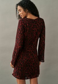 Leopardenmuster-Kleid in Rot und Schwarz, lange Ärmel, figurbetonte Silhouette, Reißverschlussdetail im Rücken, glattes Gewebe mit leicht durchscheinender Textur.