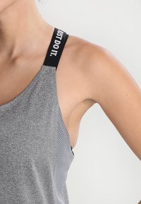 Grå atletisk tanktop med et åndbart mesh-design. Har sorte stropper med hvid tekst "JUST DO IT." som viser branddetalje.