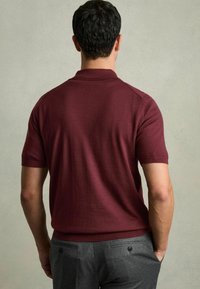 Cămașă polo burgundă cu mânecă scurtă, dotată cu guler și manșete ribbate, combinată cu pantaloni gri ce prezintă buzunare laterale și accente cu butoane.
