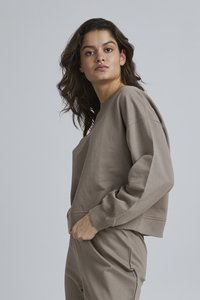Felpa corta marrone con vestibilità rilassata, polsini a costine e scollo a girocollo, realizzata in tessuto morbido. Abbinata a pantaloni coordinati.