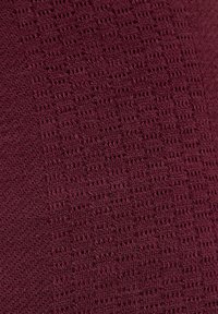 Bordowy dzianinowy materiał z fakturowanym wzorem zawierającym małe geometryczne wycięcia oraz różne rozmiary ściegów w całym materiale.