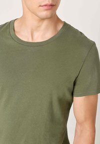 Alyvuogių žalia trumpomis rankovėmis marškinėliai su apvalia iškirpte, pagaminti iš minkštos medžiagos, pasižymintys lygiu paviršiumi ir paprastu dizainu.