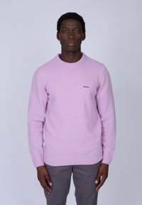 Pull en tricot rose clair avec un col rond classique et des poignets côtelés, présentant un petit logo brodé sur la poitrine.